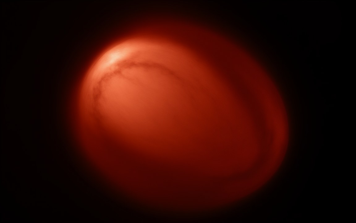 A huge red star seen through a dim reddish haze of dust around it, an impression of one of the largest known stars, the red supergiant WOH G64.